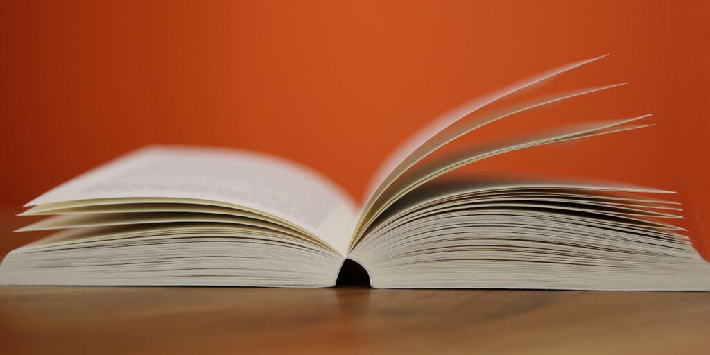 An open book with pages turning against a vibrant orange background, symbolizing knowledge and education.